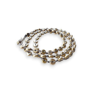 The ANN LIGHTFOOT Intermittent Brass Disk Braided Wrap Bracelet features a meticulously braided light gray cord interspersed with numerous small, golden brass disks. The bracelet, secured with a sterling silver clasp, showcases a continuous textured pattern that highlights the natural luster and smooth finish of the brass disks against the minimalist background.