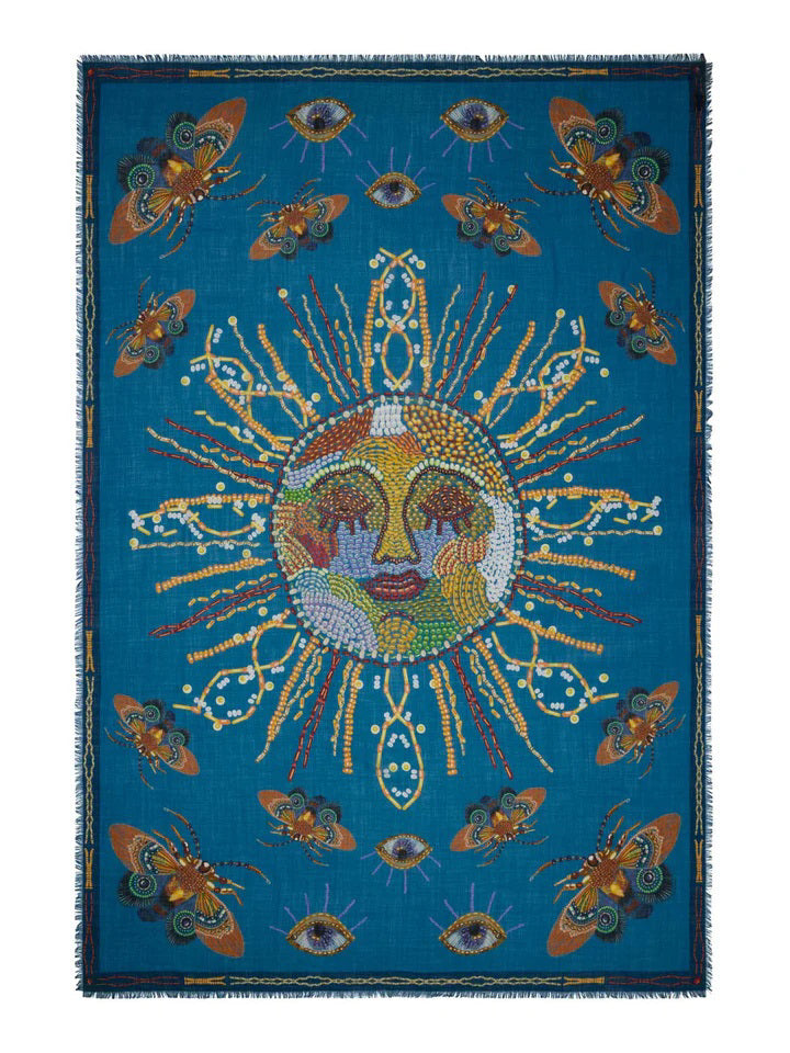 The FRANCO FERRARI - EMBROIDERED SUN WOOL SCARF by FRANCO FERRARI, made in Italy, features a central embroidered sun with rays crafted from various beads and patterns. Surrounding the sun are intricate designs of eyes, butterflies, and abstract motifs, all set against a vibrant blue background with a decorative border.