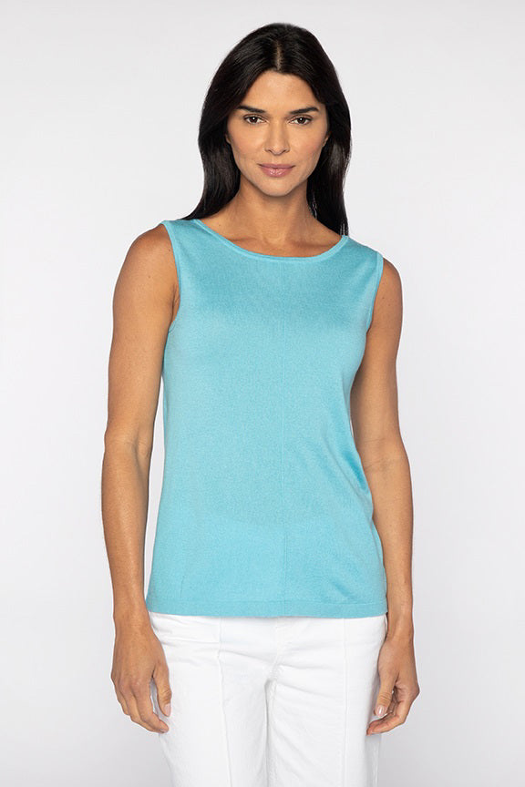 A person with long dark hair in a sleeveless turquoise KINROSS Cashmere Front to Back Silk Cashmere Tank and white pants stands against a plain white backdrop, looking directly at the camera with a neutral expression.