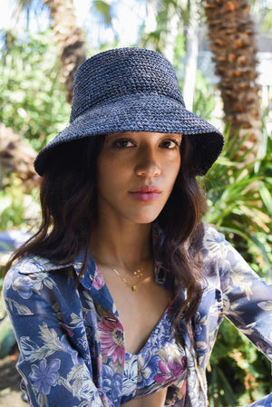 The WYETH HATS - THE TALI is a brown hand-crocheted raffia straw hat featuring a wide brim, showcased against a plain white background.