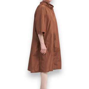 The KATHARINA HOVMAN Oversized Taffeta Dress features a long, flowing beige design with subtle sheen and elegant drape, complete with soft folds and side seam pockets. Its lightweight fabric provides airy movement, embodying a simple and timeless elegance.