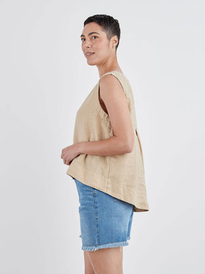 The CUT LOOSE - HI LOW TANK, a sleeveless white linen blouse with a round neckline, is displayed on a white hanger against a light gray wall. Perfect for summer wear, this breathable top by CUT LOOSE features a loose fit and an elegant high-low hem that is shorter in the front and longer in the back.