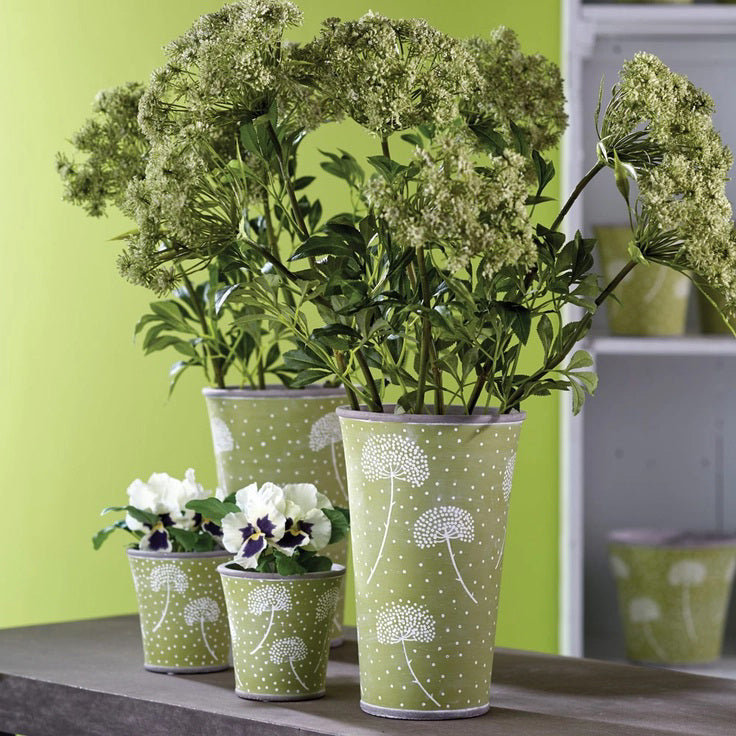 A display of realistic artificial BLOSSOM BUD STEM 24 flowers from NAPA HOME AND GARDEN in tall, green, polka-dotted pots featuring white dandelion prints. Two larger pots contain lush green plants with clusters of small flowers, while two smaller pots hold white flowers with purple centers. Ideal for home decor and available for instore pickup, they are arranged on a gray surface.