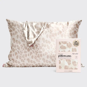 A satin pillowcase with a beige and white leopard print design is displayed against a plain background. To the right of the luxurious pillowcase is its packaging, which reads "SATIN PILLOWCASE" by KITSCH and highlights its 600-thread count and benefits for frizz-free hair and healthy skin.