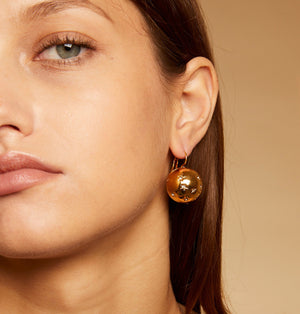 The GAS BIJOUX - COMET GOLD EARRINGS are a pair of round gold-plated earrings adorned with star-shaped Swarovski engravings. They feature a shiny finish and clasp hooks for attachment, presented against a plain white background.