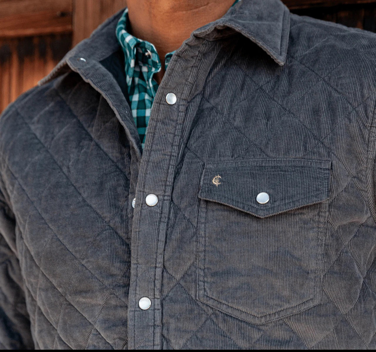 A man with short, curly hair and a beard wears the CRIQUET - CORDUROY QUILTED SHACKET by CRIQUET and blue jeans, standing against a white background while smiling and looking to his right.