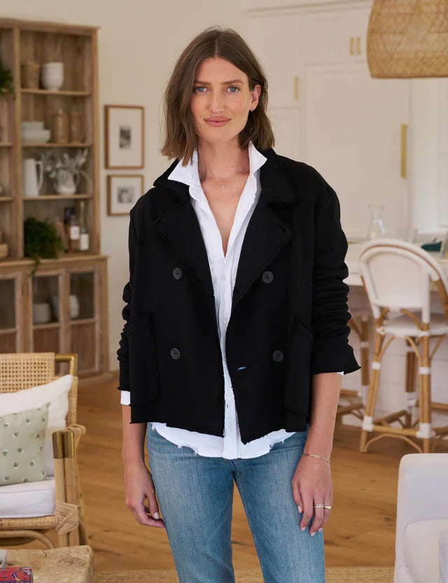 The FRANK &amp; EILEEN - MINI BELFAST CROP PEACOAT IN BLACK by FRANK &amp; EILEEN features a double-breasted design with sleek horn buttons. It comes complete with two front pockets and is showcased against a plain white background. The left sleeve is slightly rolled up, adding a touch of casual elegance reminiscent of its Mini Belfast peacoat inspiration.