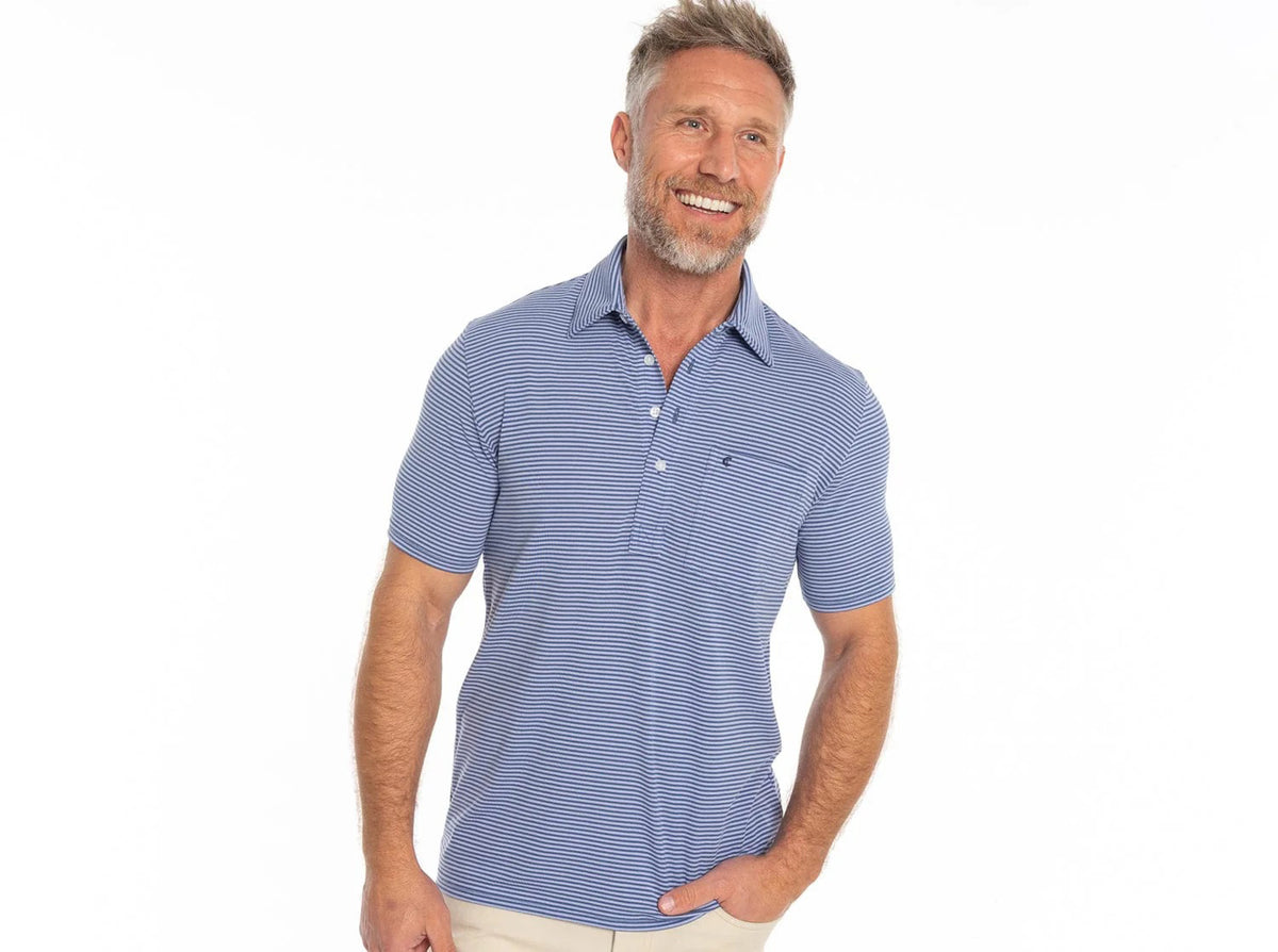 A smiling man with short gray hair and a beard wears the CRIQUET Performance Players Shirt in Ferrel Stripe Blue and light pants, standing against a plain white background.