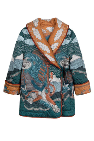 A person wears the SABINA SAVAGE - THE SNOW LION QUILTED JACKET from SABINA SAVAGE ENGLAND, featuring a colorful, intricately designed nature-themed pattern with trees, sky, and animals. Reminiscent of a reversible silk twill jacket, it features a wide collar, contrasting orange inner lining, and large pockets. The person is shown from the shoulders down.