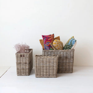 Three SMALL WOVEN WICKER RATTAN BASKETS WITH HANDLES from CREATIVE COOP of varying sizes are placed vertically in a straight line against a white background. Each basket features intricately woven rattan material and an open top.