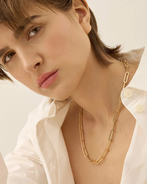 The JENNYBIRD ANDI SLIM NECKLACE is a high-polish gold paperclip necklace featuring elongated, rectangular links, showcased against a plain white background. With an elegant design of alternating small and larger links, it offers adjustable length for a refined and modern appearance.