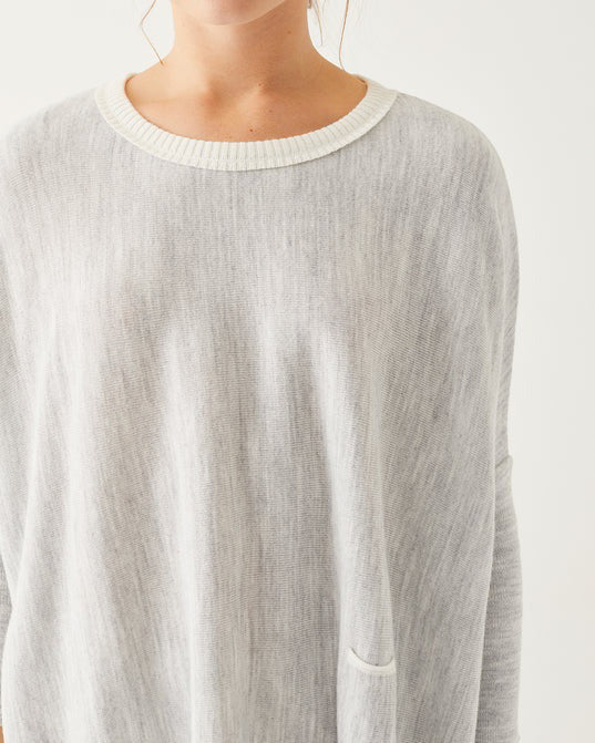 A woman with curly hair smiles while wearing a loose, gray Catalina Crewneck Oversized Sweater by MER SEA. She stands in front of a plain white background.