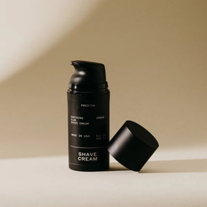 A black cylindrical bottle of PRESTON - SHAVE CREAM with a matte finish, labeled "Preston" at the top. The label reads, "Soothing Aloe Shave Cream," "Leather," and "Made in USA." Featuring a cruelty-free formula designed for razor burn prevention, the bottle has a sleek design against a neutral background.