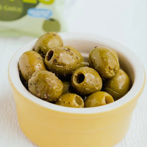 A light green packet of OLOVES - BASIL & GARLIC natural green pitted Greek olives by POSHI, flavored with basil and garlic. The packaging showcases a cartoonish olive graphic and emphasizes: "Low Calorie Snack," "New Greek Olives," "Kids & Adults Love 'Em," "Gluten-Free Vegan Snacks," and "30g | 1.1oz.