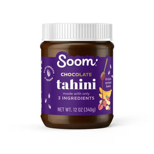 The SOOM FOODS - SOOM CHOCOLATE TAHINI comes in a brown jar with a white screw-on lid. The label displays nutrition facts, including serving size, calories, and amounts of total fat, cholesterol, sodium, carbohydrates, and protein. This chocolate spread is labeled kosher, vegan, and gluten-free.