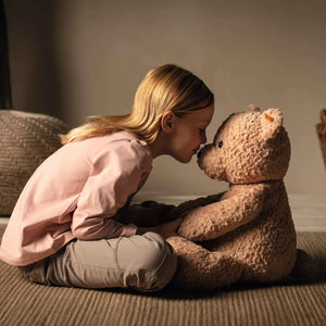 The STEIFF XL JIMMY TEDDY BEAR features a cuddly light brown coat and sits upright against a white background. Its black button eyes, black nose, and small yellow tag in its left ear make it an unforgettable gift to cherish forever.