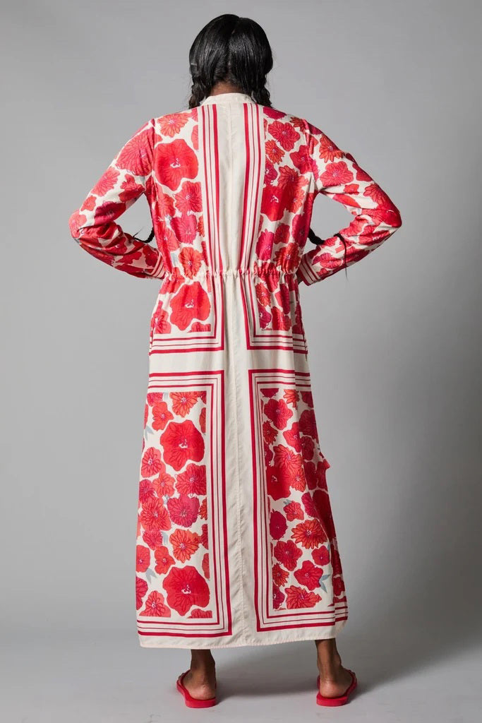 A barefoot person stands against a gray backdrop wearing the HOPE FOR FLOWERS - BAND COLLAR SHIRTDRESS, which features a cream background with vertical stripes, long red florals, a cinched waist, and long sleeves.