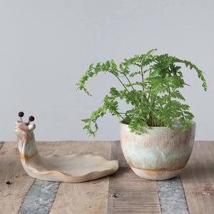 The STONEWARE SNAIL PLANTER by CREATIVE COOP features a stoneware base with an earthy texture and reactive glaze. Its snail body forms the base, while a round pot acts as the shell, complete with metal springs and pom-poms for whimsical antennae.