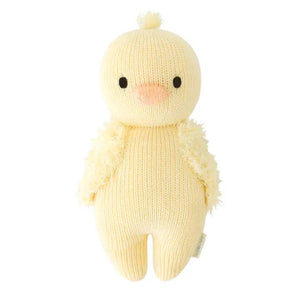 A soft, knitted yellow plush toy named "CUDDLE + KIND - HANDMADE BABY DUCKLING" by the brand CUDDLE & KIND, featuring a round head and body and viewed from the back. This charming toy has small wings and a tuft of 100% cotton yarn on its head, resembling a hand-knit baby chick while providing fair trade income to artisans.