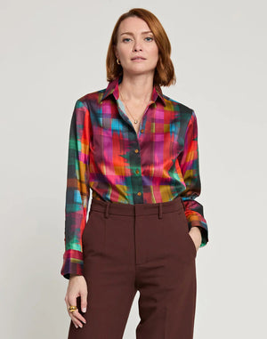 A person with shoulder-length auburn hair is shown from the back, wearing the HINSON WU - Margot Long Sleeve Satin Shirt in Festive Plaid. The multicolored plaid shirt features a collar and includes shades of red, green, yellow, and pink. It is paired with brown pants.