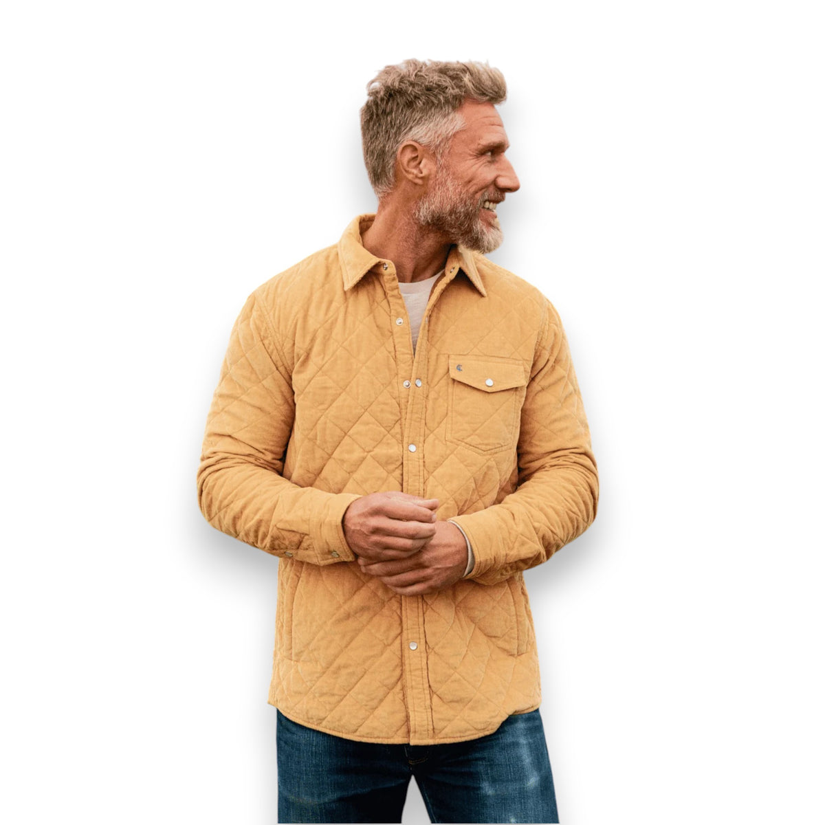 A man with short, curly hair and a beard wears the CRIQUET - CORDUROY QUILTED SHACKET by CRIQUET and blue jeans, standing against a white background while smiling and looking to his right.