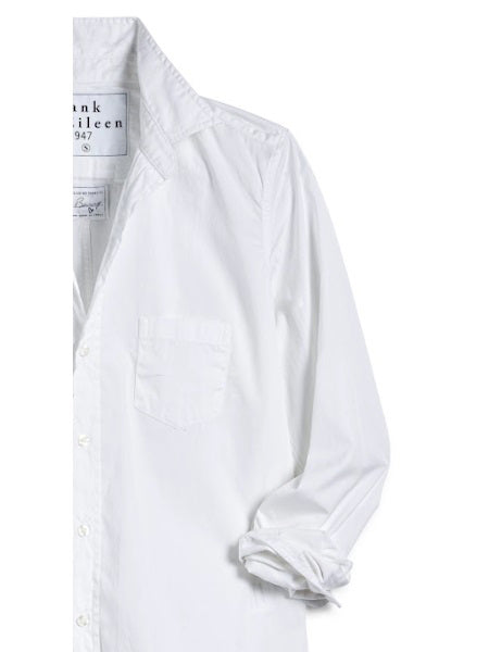 A man with short curly hair wears the FRANK &amp; EILEEN LUKE Men&#39;s Button Up Shirt in Classic White Poplin (sleeves rolled), paired with light blue ripped jeans and a watch, smiling slightly against a plain background.