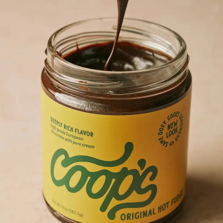 A jar of COOP'S - ORIGINAL HOT FUDGE is displayed with a dark brown lid and yellow label. The lid features a drip effect, resembling fudge oozing down the sides. The label boasts "Deep Rich Flavor, high-quality European chocolate with pure cream." This artisanal treat has a net weight of 10 ounces (283.5g).