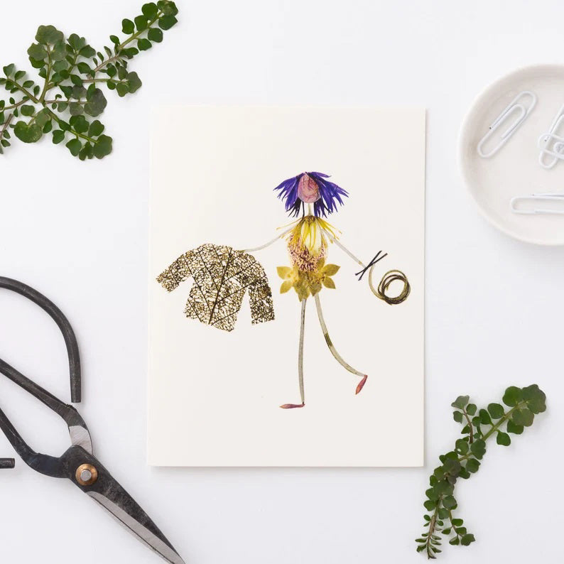 The KNIT AND PURL GREETING CARD by PETAL PEOPLE PRESS features an artful arrangement of vibrant dried flower petals, leaves, and stems on a pristine white background. A delicate skeleton leaf enhances its enchanting appeal, with the presence of tweezers and small scissors hinting at a whimsical crafting or botanical project.