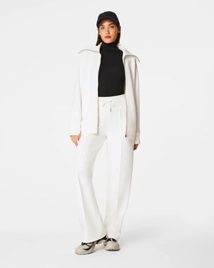 A person wearing a black long-sleeve top and high-waisted SPANX AirEssentials Luxe Straight Leg Pants in white stands with their back to the camera, highlighting the pant's design and fit, made from super-soft spacer fabric.