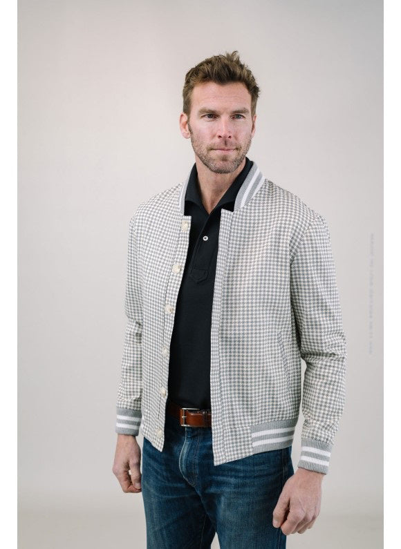 A man with short brown hair and a trimmed beard models the EDWARD ARMAH Pima Cotton Tailored Polo Shirt in white with light-colored pants, standing against a plain light background, one hand in his pocket, looking to the side.