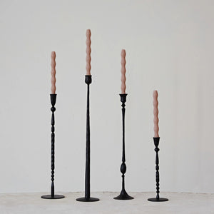 A set of four HAND FORGED CAST IRON TAPER HOLDERS by CREATIVE COOP, paired with beige spiral candles, stand on a plain, light-colored surface against a light gray background. The varied designs and heights of these tall black candlesticks add an elegant and minimalist aesthetic while infusing rustic charm into the scene.