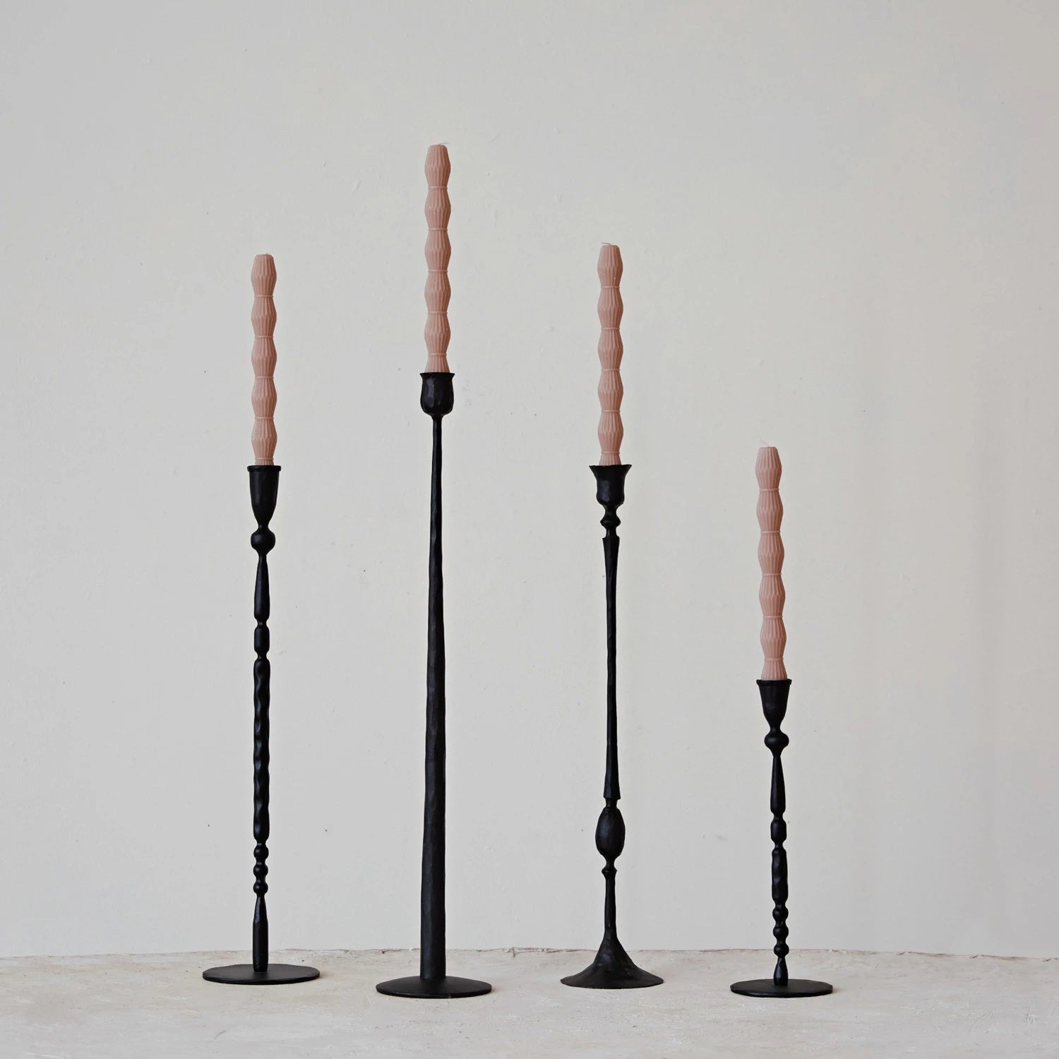 Four elegant CAST IRON TAPER HOLDER 24" by CREATIVE COOP cradle pink spiral candles in varying heights. Each hand-forged piece stands against a white backdrop on a light surface, showcasing exquisite craftsmanship.