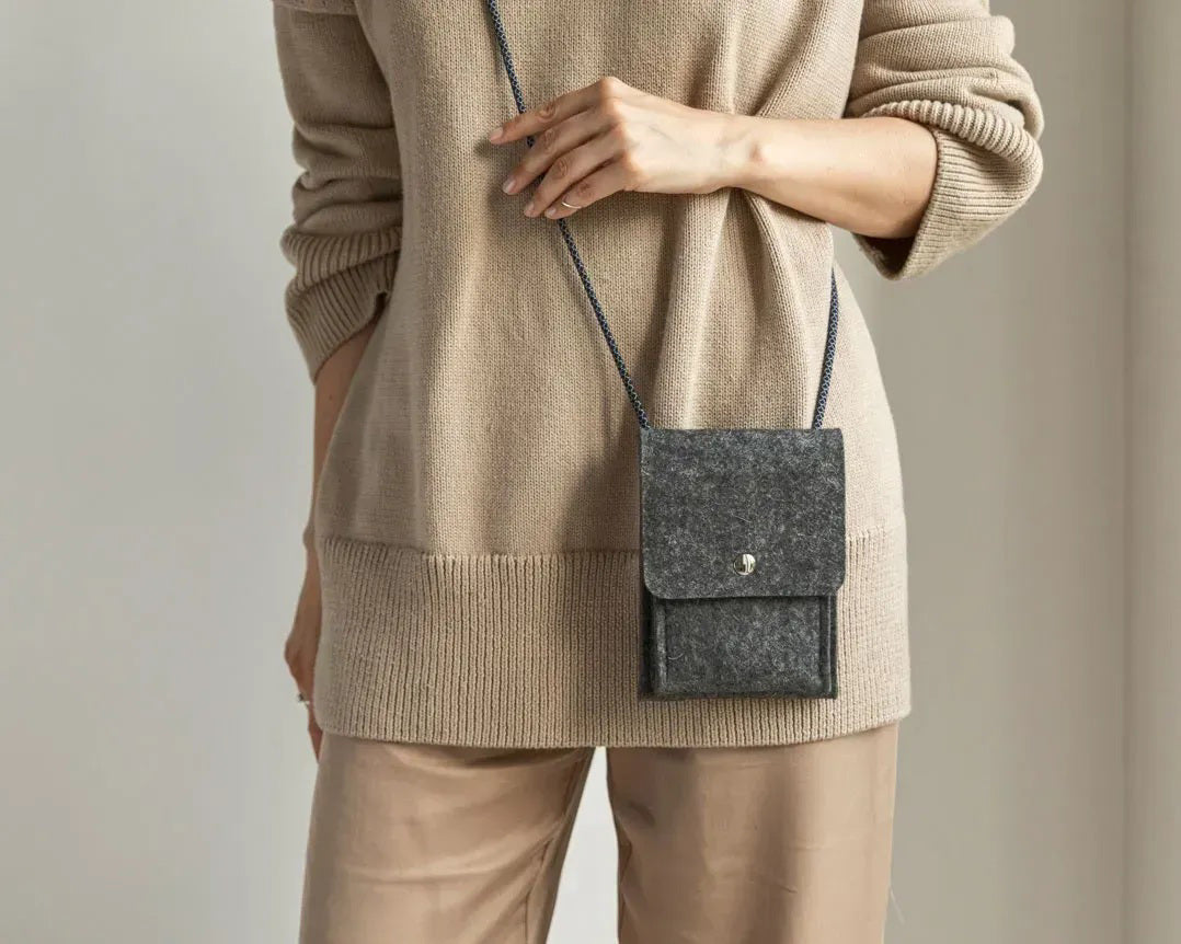 A person in a loose gray shirt and taupe pants carries the WOOLBERRY WOOL FELT PHONE BAG—a pink crossbody with a flap and silver chain—over their shoulder, showing only their torso and part of their arms.