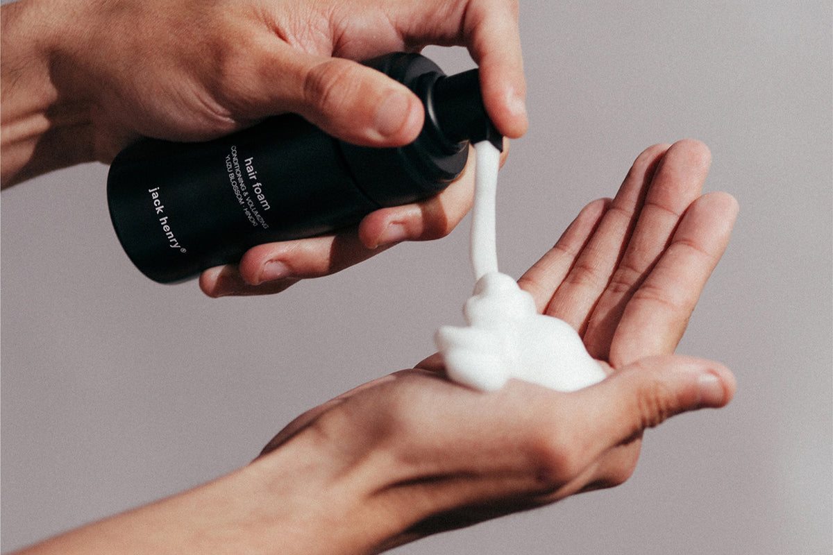 A sleek black bottle of JACK HENRY - HAIR FOAM, featuring minimal white text on the front, casts a shadow on a white background.