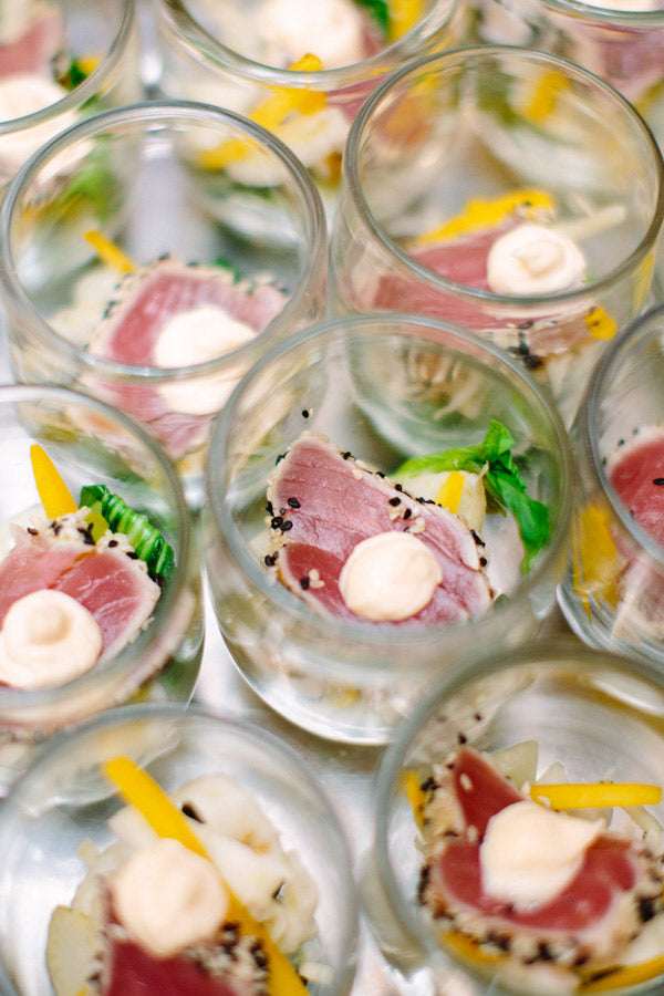 Several small glass cups filled with seared tuna slices topped with a dollop of creamy sauce, served on a bed of vegetables and garnished with thin yellow pepper strips.