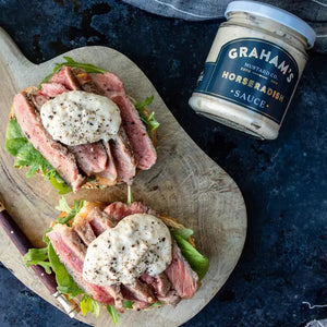 A jar of Graham's Irish Horseradish Mustard with a white lid. The label is navy blue with gold and white text, stating "Graham's Mustard Co. Estd 2014" on top and "Irish Horseradish Mustard" on the bottom. Perfect for pairing with roast beef, this creamy light beige sauce has earned great taste awards.