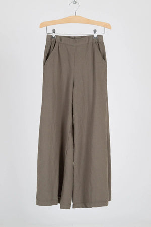 A pair of CP SHADES - WENDY PALAZZO PANT in beige is hanging on a wooden hanger against a light gray background. These cotton pants from CP SHADES feature an elastic waistband and handy side pockets, designed with a high-rise and wide-leg silhouette.