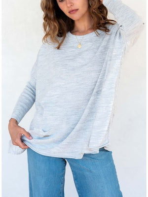 A woman with long hair wears a bright orange poncho over a white collared shirt and blue jeans. She is adjusting the poncho with her hand while smiling against a plain white background, showcasing a versatile look that can easily replace your favorite MERSEA Catalina Crewneck Sweater for any occasion.