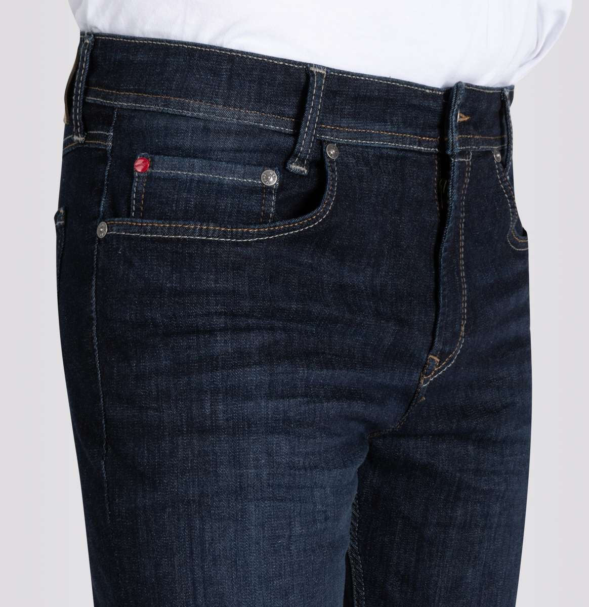 Close-up of a person wearing MAC Ultimate Driver Jeans in Rinsed Wash 3D, a men&#39;s modern fit in dark blue stretch denim by MAC, featuring contrast stitching, a coin pocket with red detail, and a white shirt tucked in.