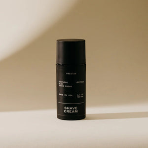 A black cylindrical bottle of PRESTON - SHAVE CREAM with a matte finish, labeled "Preston" at the top. The label reads, "Soothing Aloe Shave Cream," "Leather," and "Made in USA." Featuring a cruelty-free formula designed for razor burn prevention, the bottle has a sleek design against a neutral background.