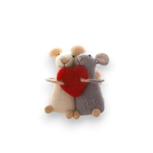 The WOOL FELT MICE WITH HEART ORNAMENT from CREATIVE COOP features a pair of wool felt mice, one in white and the other in gray, holding a red heart ornament together beneath a slender horizontal brown beam against a plain white background.