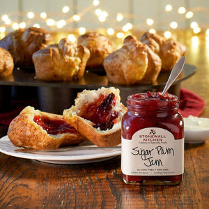 A jar of STONEWALL KITCHEN - SUGAR PLUM JAM is showcased, ideal for holiday treats. The label describes it as "a classic fruit spread" and has a net weight of 354g (12.5 oz). The jar comes with a green lid, and the jam inside is a deep red color.