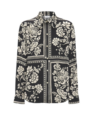 A woman with blonde, chin-length hair is wearing the MIRTO 1956 - BLACK AND WHITE PRINT FLUID BLOUSE. Embracing the intricate flower squares patchwork print of MIRTO fashion, she stands neutrally against a plain white background.