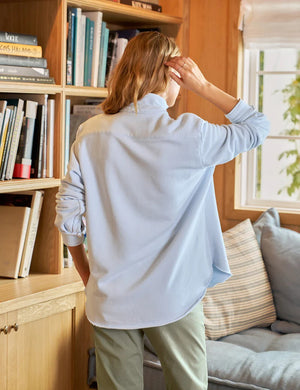 A light blue long-sleeve button-up shirt with a collar and single chest pocket is laid flat, its sleeves casually rolled up to highlight the relaxed fit. The inner label reads "FRANK AND EILEEN." Product: EILEEN SWEATSHIRT BUTTON UP IN ICE by FRANK & EILEEN.