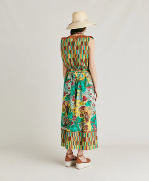 The MOMONI - IRIS SKIRT from MOMONI is a long, high-waisted skirt made from printed poplin. It features a vibrant floral and botanical design in green, yellow, red, and brown. The hemline and constructed waistband are accented with a contrasting striped pattern in similar hues. This skirt boasts a flowy, A-line silhouette.