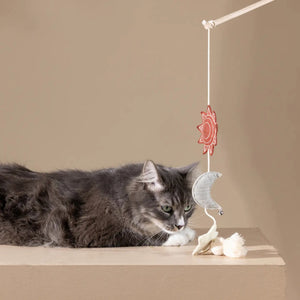 The PET SHOP BY FRINGE STUDIO's HAPPY SKIES CAT TEASER TOY features a wooden stick with a hanging toy: red star, silver crescent moon with bell, and beige star—linked by strings and ending in a tassel for interactive play to engage your cat.