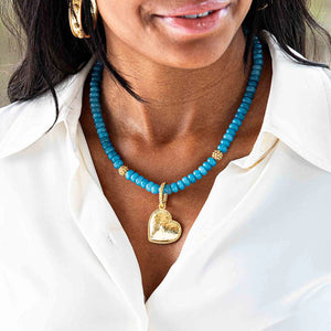 Close-up image of a woman wearing the CAPUCINE DE WULF - BERRY SINGLE STRAND NECKLACE, made of blue beads and pearls with gold spacers. She is wearing a white top. Only the lower part of her face and the upper part of her chest are visible.