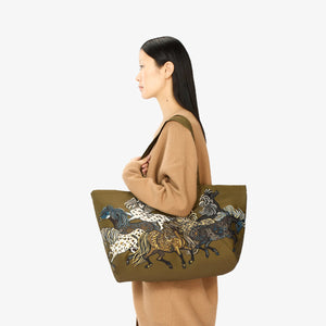 The INOUI EDITIONS MAXI WESTERN SHOPPER BAG by INOUI is a brown tote bag adorned with a design showcasing multiple horses in various poses, painted in shades of brown, black, and white with intricate detailing. Made from recycled polyester, this eco-friendly bag features two shoulder straps and a smaller pair of handles for versatile carrying options.