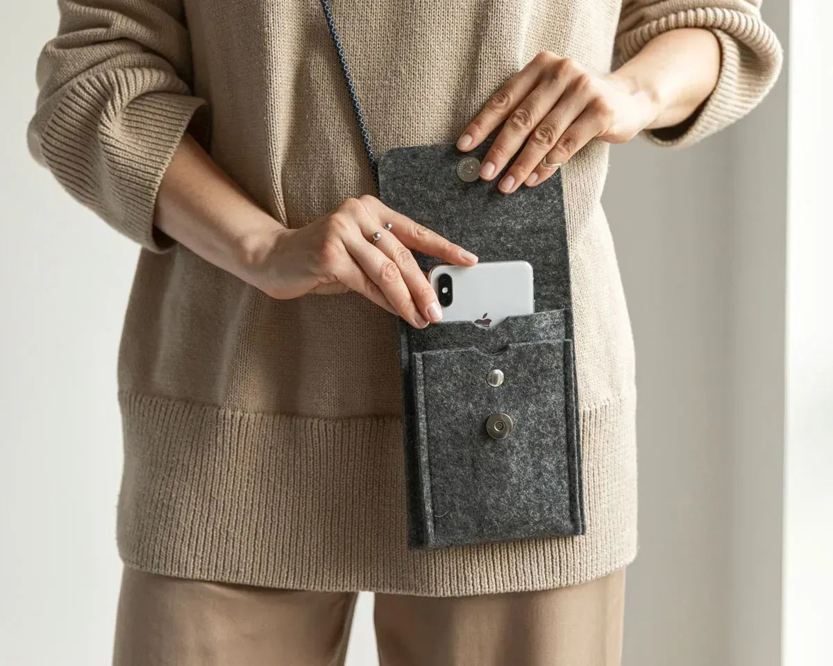 A person in a loose gray shirt and taupe pants carries the WOOLBERRY WOOL FELT PHONE BAG—a pink crossbody with a flap and silver chain—over their shoulder, showing only their torso and part of their arms.