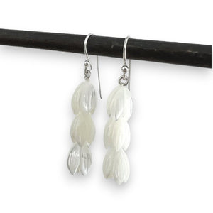 A pair of ANN LIGHTFOOT - TRIPLE TULIP MOTHER OF PEARL EARRINGS hangs from a black rod against a plain light gray background. Each earring features three petal-shaped segments stacked vertically, creating a cascading effect, and is adorned with sterling silver earwires for added elegance.